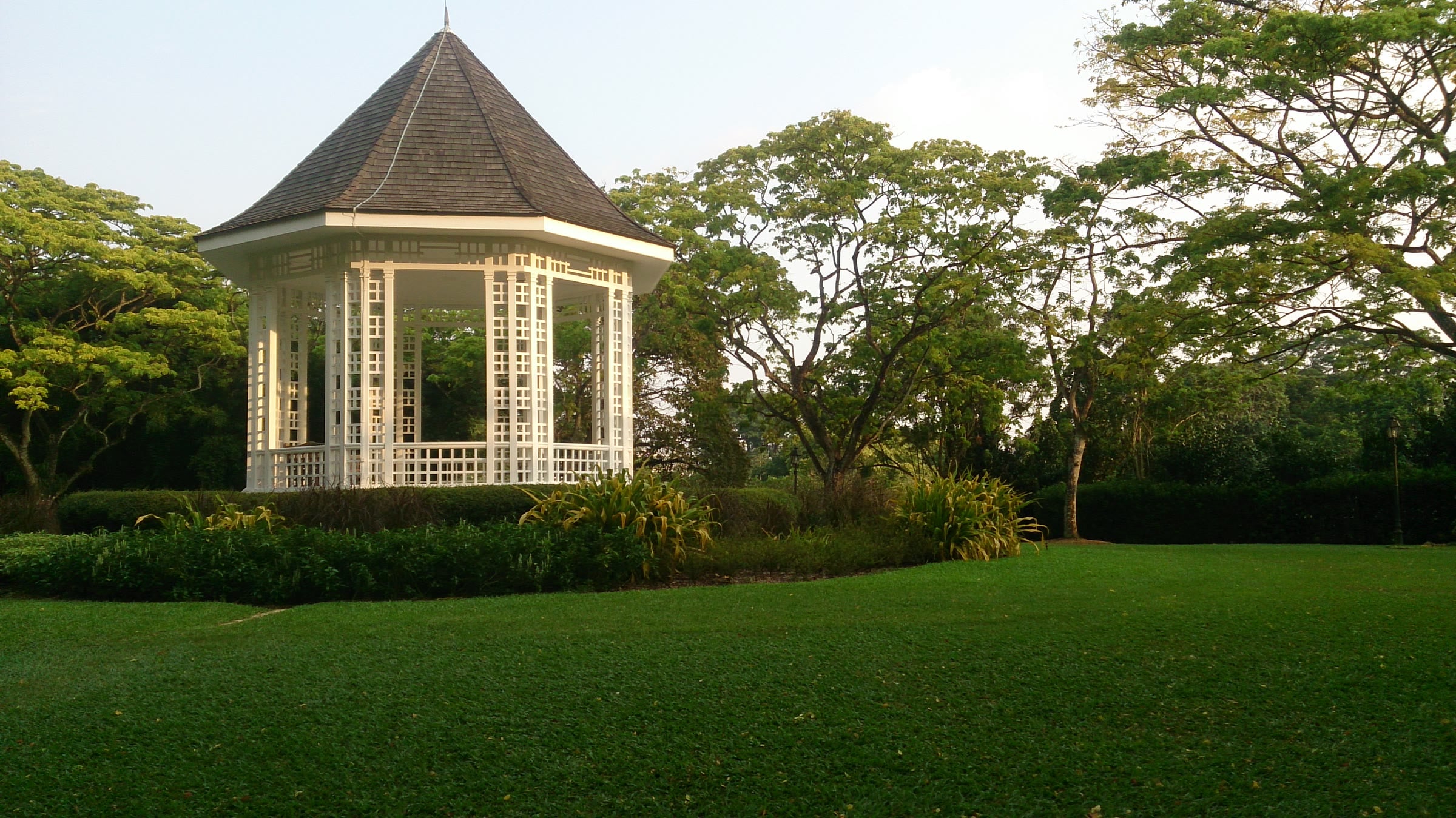 The bandstand at the Singapore Botanic Gardens in low evening light, beneath mature trees.